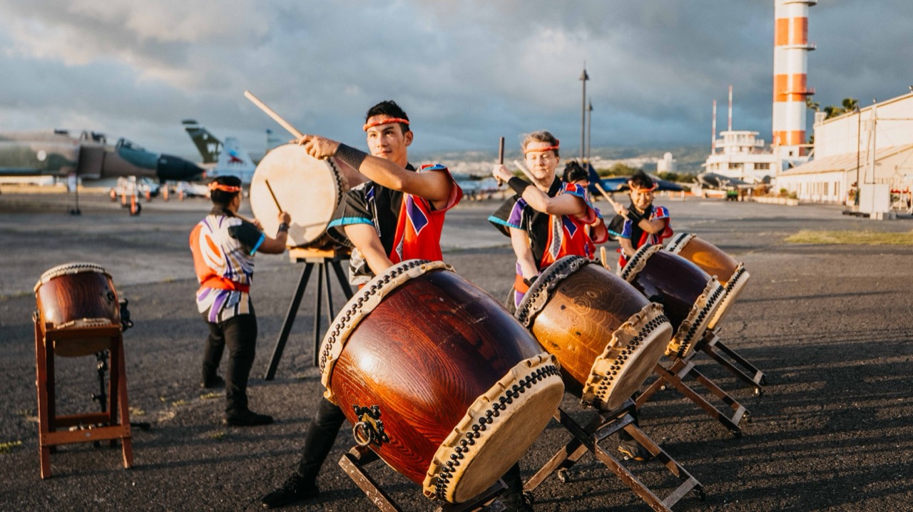 Sho’on Shibata performing with Taiko Center of the Pacific outdoors beside aircraft